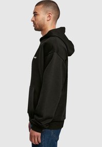 Black hooded sweatshirt made of fleece, featuring a kangaroo pocket, ribbed cuffs, and a relaxed fit, worn with blue jeans.