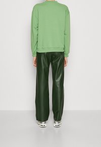 Sudadera verde con cuello redondo y hombros caídos, combinada con pantalones de imitación cuero verdes de cintura alta. Ambas prendas son de un solo color.