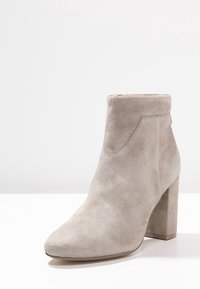 Stivaletto in suede grigio con punta appuntita, gambale corto e tacco alto chunky. Presenta una chiusura con zip laterale e una texture liscia.