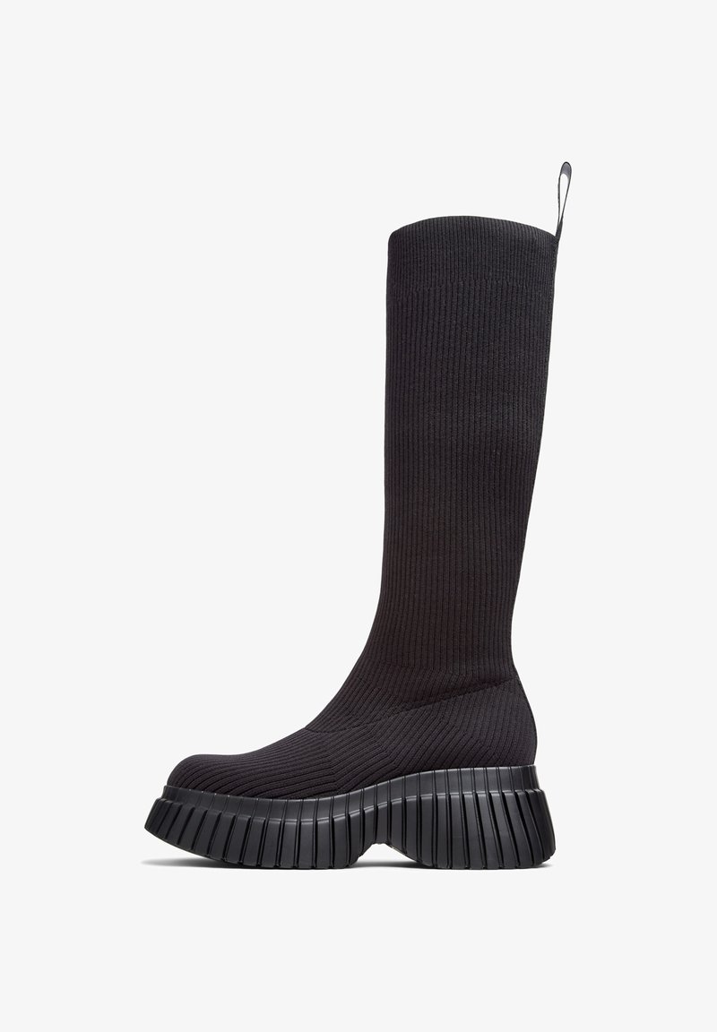 Botas negras de punto hasta la rodilla con textura acanalada, que cuentan con una suela gruesa y estriada para mayor agarre y estabilidad.