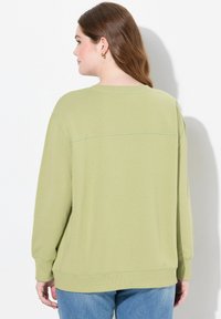 Felpa verde chiaro con una vestibilità morbida, polsini a coste e un dettaglio di cucitura sulla schiena, abbinata a jeans blu.