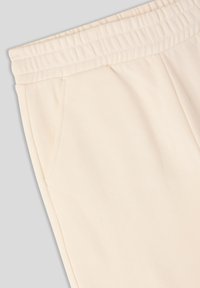 Jasne kremowe dresy z elastycznym pasem, bocznymi kieszeniami i miękką, gładką teksturą. Brak widocznych wzorów lub akcentów.