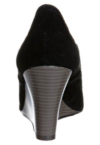 Svart mocka högklackad sko med spetsig tå och en slät, texturerad brun kilklack, med böljande linjer och en elegant design.