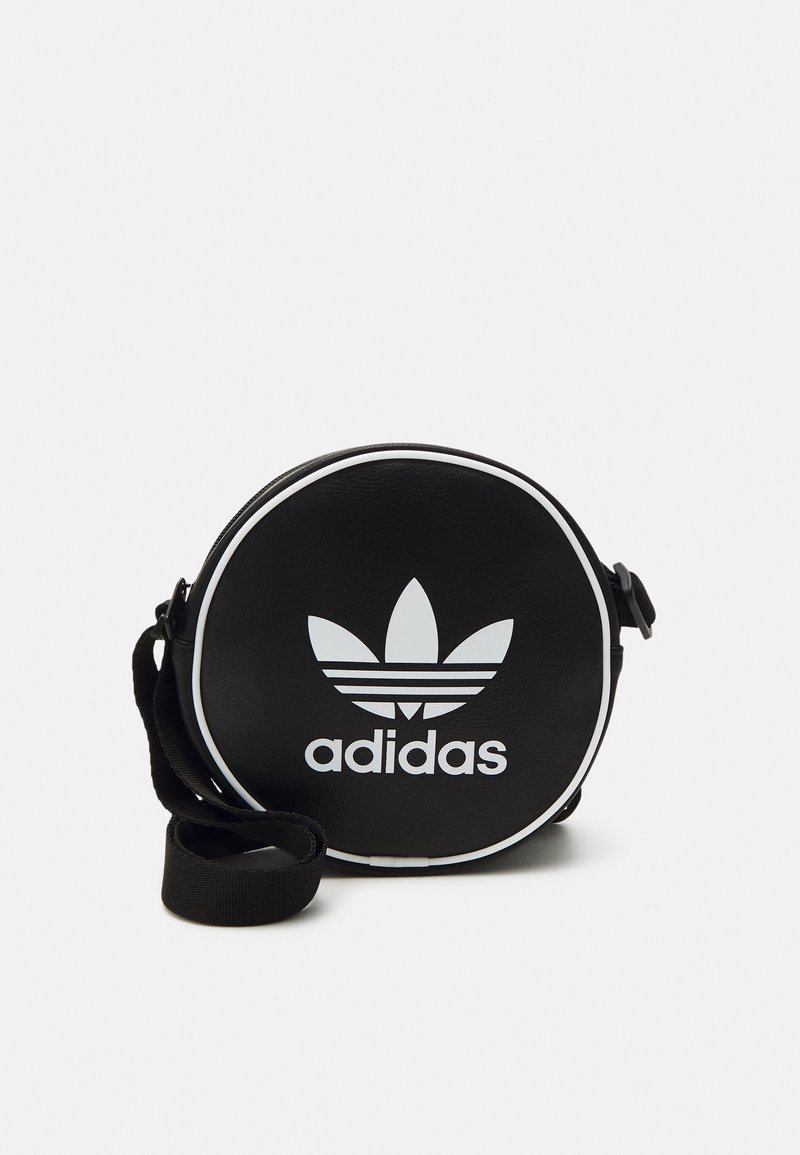 Černá kulatá taška z umělého materiálu s bílými detaily a logem Adidas. Má nastavitelný popruh pro nošení.
