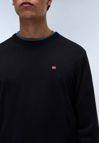 Jersey negro con cuello redondo, que presenta una pequeña bandera noruega bordada en el pecho. La textura parece suave y lisa.