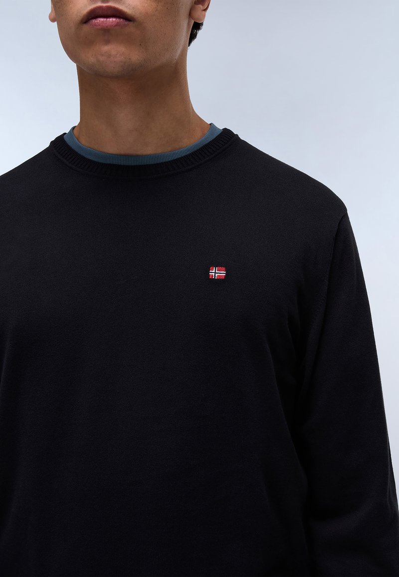 Maglione nero a maglia con scollatura rotonda, caratterizzato da una piccola bandiera norvegese ricamata sul petto. La trama appare liscia e morbida.