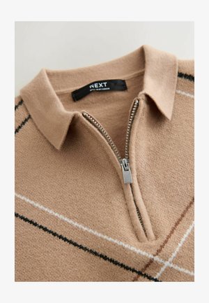 Beige gebreide pullover met een kraag, halve ritssluiting en contrasterende diagonale strepen in zwart en wit. Zachte textuur. Merkenlabel: NEXT.