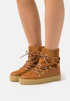Bottes en cuir brun et suède jusqu'à la cheville avec une semelle texturée brun clair, dotées de quincaillerie dorée, de lacets et d'un col rembourré.