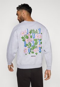 Felpa grigia con un design floreale sul retro, caratterizzata da fiori rosa, foglie verdi e scritte blu con la parola "JUVENTUS."