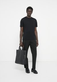 Svart bomulls t-shirt, mörkgröna byxor och en svart läder tote-väska med vertikala sömmar, bärs med svarta skor. Enkelt, modernt design.