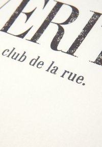 Hvidt stof med trykt sort tekst. Det store "VERI" er fremtrædende, med "club de la rue" i mindre skrifttype nedenfor. Teksten har et slidt udseende.