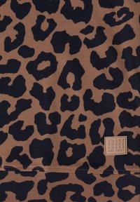 Tissu marron avec des taches de léopard noires irrégulières et un petit écusson carré avec du texte dans le coin inférieur droit.