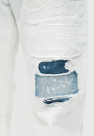 Λευκό τζιν παντελόνι με φθαρμένες τρύπες που έχουν ραφτεί με πιο σκούρο και ανοιχτό μπλε τζιν ύφασμα στον μηρό.