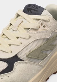 Béžová a krémová teniska s panelmi z sieťoviny a semišu, béžové šnúrky, tmavosivé štítok na jazyku s logom Hi-Tec a viditeľná textúrovaná podrážka.