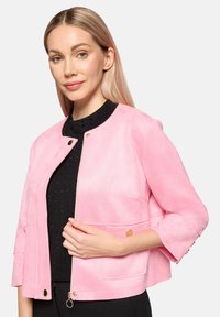 Veste en suédine rose avec un col rond, des manches trois-quarts et des accessoires en métal doré. Comprend des fermetures à pression et des poches latérales.