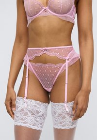 Σετ ροζ δαντελένια εσώρουχα με πουά σχέδιο, διαφανές ύφασμα, λεπτομέρειες με βολάν και ράντες ζαρτιέρας συνδυασμένο με λευκές δαντελένιες κάλτσες μέχρι το μηρό.