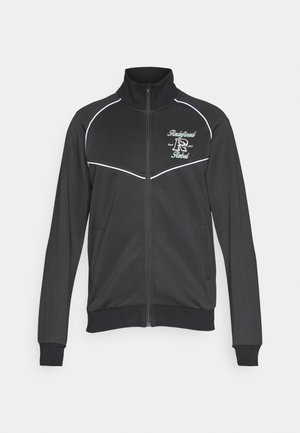 Czarna kurtka zapinana na zamek z białymi lamówkami, wysokim kołnierzem i dwiema bocznymi kieszeniami. Na przodzie haftowane logo w zielonym i białym kolorze.