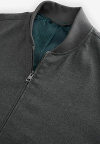 Graue Bomberjacke mit einem Frontreißverschluss, geripptem Kragen und einem strukturierten tealfarbenen Futter mit geometrischem Muster. Glatte Außenfläche.