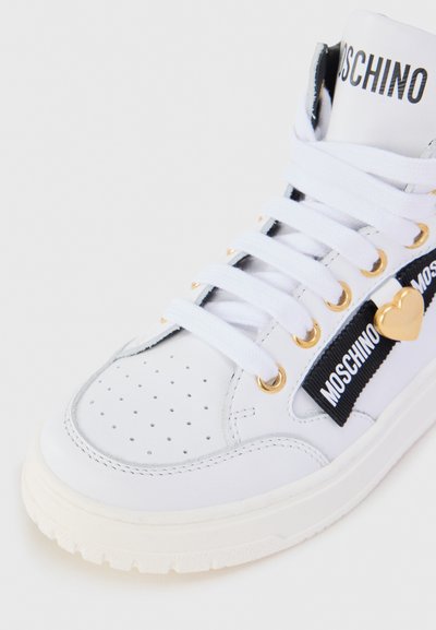 White high-top sneaker made of leather with perforated details, gold eyelets, white laces, and black ribbon featuring "Moschino" branding.