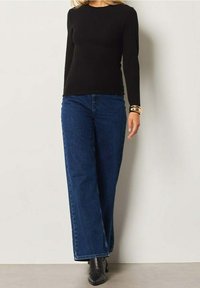 Haut noir à manches longues, jean en denim bleu taille haute, coupe jambes larges, et bottines noires. Design simple sans motifs visibles.