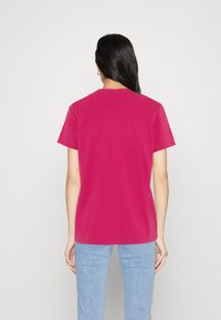 Pink short-sleeve t-shirt with a round neckline, displayed from the back. Cotton material with a smooth texture, paired with light blue jeans.