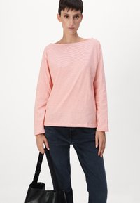 Top de manga larga rosa claro con finas rayas blancas, escote ancho y corte relajado, combinado con jeans oscuros y un bolso tote negro.