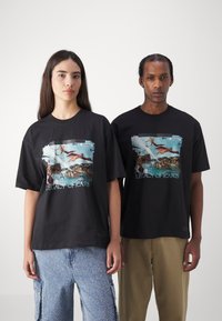 Black cotton T-shirts feature a graphic print in blue and brown depicting a scene with figures and text "LEGACY OF ICARUS." Loose fit.