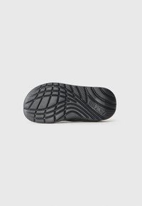 Semelle de chaussure en caoutchouc noir avec des motifs de texture, comprenant des rainures et des crêtes pour une meilleure adhérence, étiquetée du nom de la marque "TEXAS".
