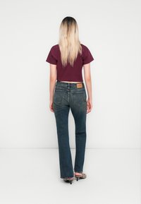 Mørkeblå bukser med vide ben og klassisk fem-lommers design, samt en brun lærreim på baksiden. Kombinert med en kortermet maroon croptop.