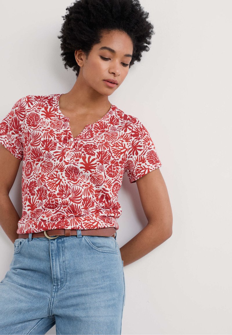 Camicia a maniche corte rossa e bianca con un motivo floreale, scollo a V e una vestibilità comoda, abbinata a jeans a vita alta di un blu chiaro.