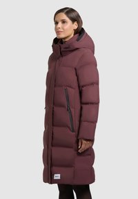 Bordo värvi sulejope põlveni ulatuva lõikega, kõrge krae ja kapuutsiga. Varustatud külje tõmblukkudega ja logomärgisega äärel. Sile tekstuur.