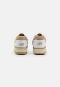 Białe i beżowe sneakersy z teksturowanym siateczkowym wierzchem, gumową podeszwą i wyraźnym logo "NB" na pięcie.