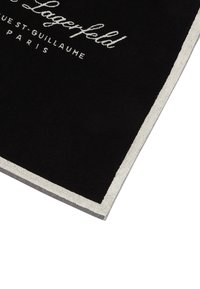 Melnā dvielī ar mīkstu tekstūru, ar kontrastējošu pelēku apmalīti. Izšūts balts logo teksts ir redzams izcili.