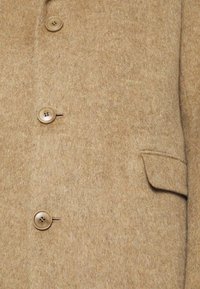 Lähi-ystäbeä beige villakangas takki, jossa on kolme nappia ja läpällinen tasku tekstuurilla varustetulla kankaalla.