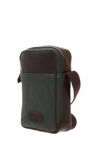 Sac messager en toile vert foncé avec des accents en cuir marron, fermeture éclair, bandoulière réglable et écusson logo à l'avant. Forme rectangulaire.