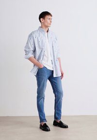 Short-sleeve, light blue striped shirt with small embroidered accents, paired with fitted light blue jeans and black loafers.