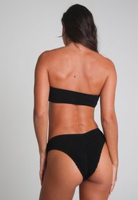 Svart stickad bikiniuppsättning med strapless topp och högmidjade underdelar. Tyget har ett texturerat mönster och en åtsittande design.