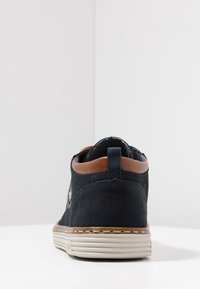 Sneaker in suede blu navy con una accentuazione in pelle marrone sul tallone, suola in gomma bianca e testurizzata, e un piccolo logo sul lato.