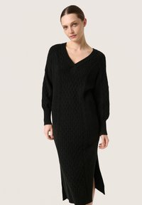 Rochie tricotată neagră, cu decolteu în V, model texturat cu cabluri, mâneci lungi puff și slituri laterale la hem. Lungime până la mijlocul gambei.