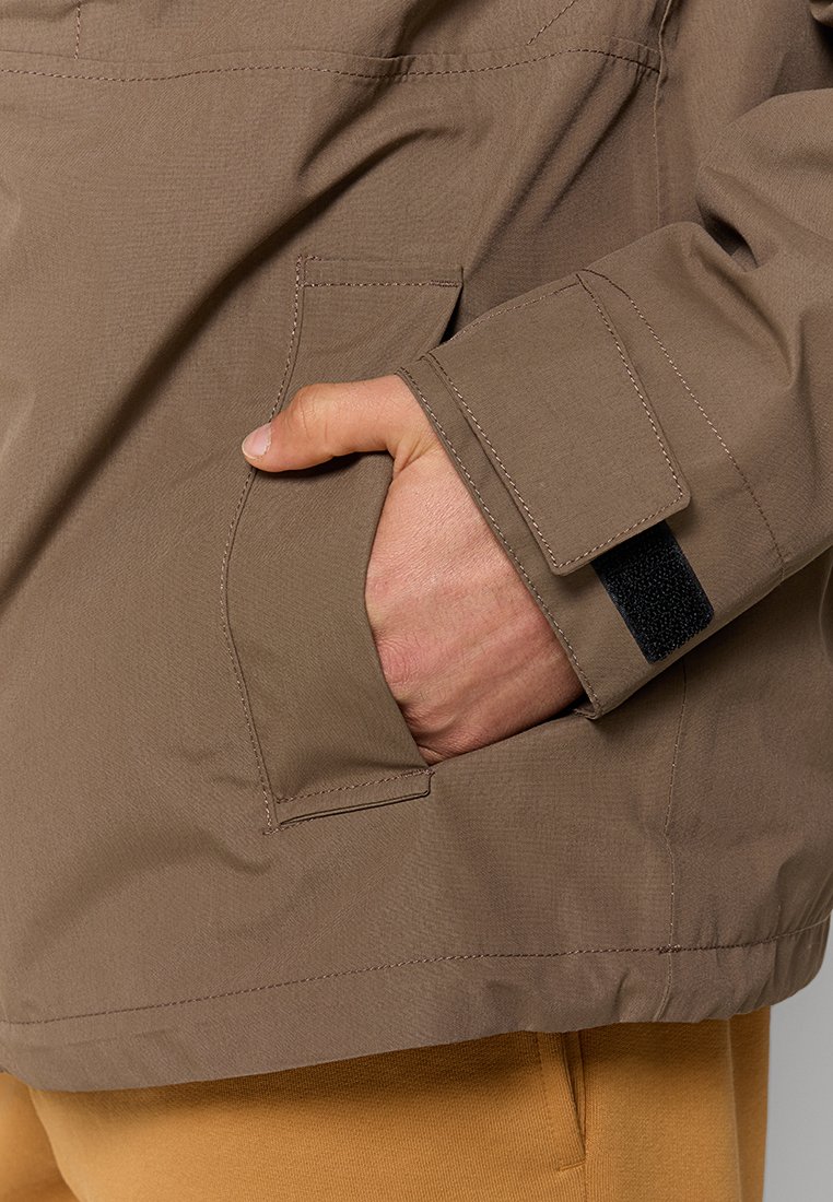 Brązowa kurtka o gładkiej fakturze, z boczną kieszenią i zapięciem na rzep przy mankiecie. Minimalistyczny design z wyraźnym przeszyciem.