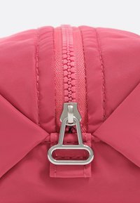 Bolso de nylon rosa con cierre central de cremallera, herrajes metálicos y acentos en ángulo a cada lado para un diseño estructurado.