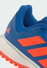 Gros plan d'une chaussure de sport bleue avec des bandes orange, un col de cheville en mesh, une semelle intermédiaire blanche et une semelle extérieure en caoutchouc orange.