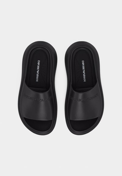 Ζευγάρι μαύρων σαγιονάρων Emporio Armani με ανάγλυφο λογότυπο στα λουράκια και επενδυμένες εσωτερικές σόλες, απεικονισμένα από πάνω σε λευκό φόντο.