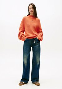 Maglione arancione oversize a coste con collo alto. Abbinato a jeans a gamba larga blu scuro con leggere sfumature e un portachiavi a forma di stella.