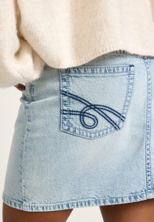 Lyseblå denimnederdel med synlige stikninger på baglommen, båret sammen med en off-white, blød og luftig sweater.