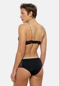 Ensemble de lingerie noire comprenant un soutien-gorge en dentelle à dos ouvert avec des bretelles satinées ajustables et un shorty taille haute assorti avec des détails en dentelle sur les côtés.