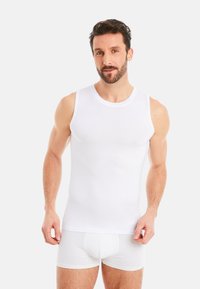 White cotton tank top with round neckline, sleeveless design, smooth texture. Worn with matching white boxer shorts.