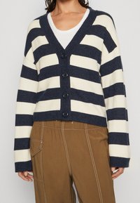 Marinblå och krämrandig cardigan med v-ringning, knäppning framtill och kort design. Mjukt stickat tyg med långa ärmar och ribbade muddar.