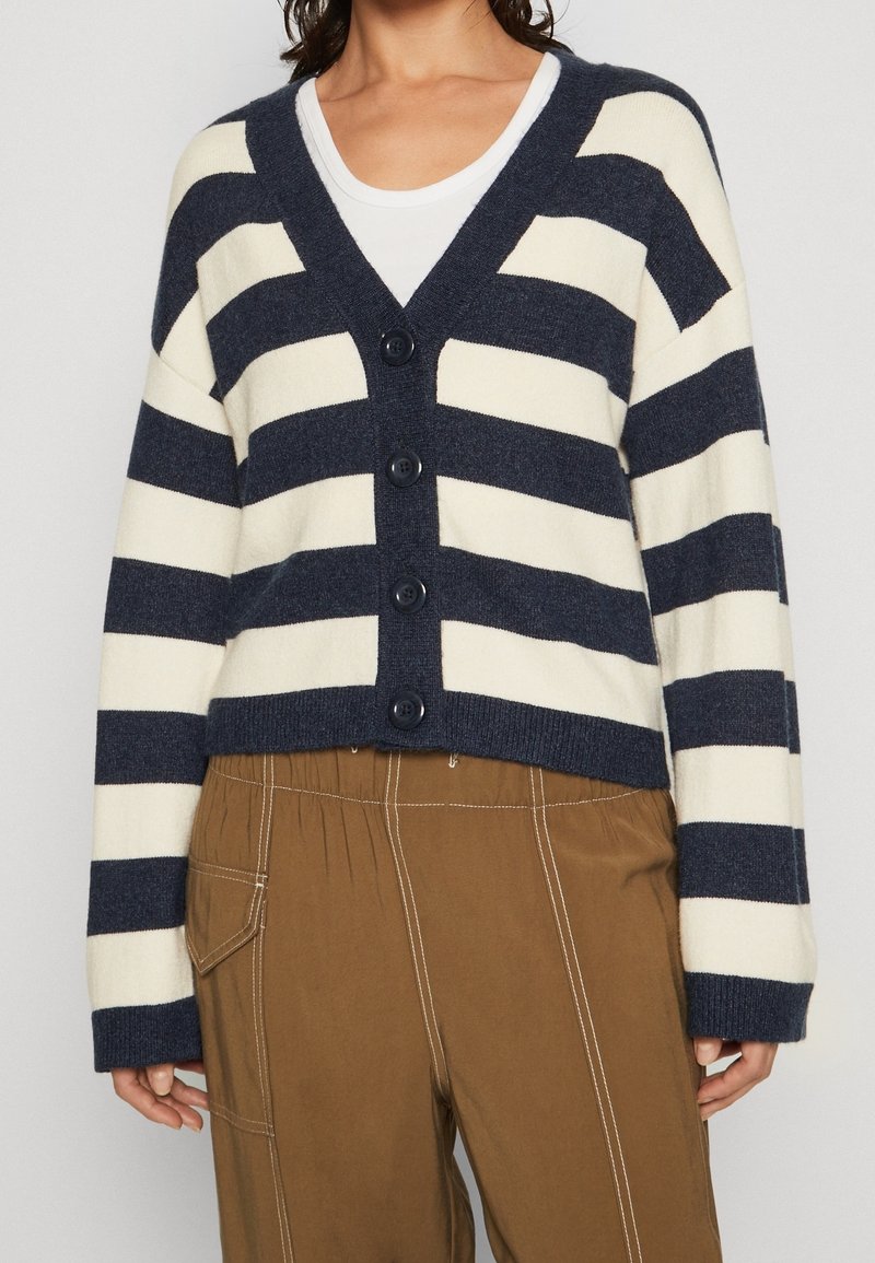 Marinblå och krämrandig cardigan med v-ringning, knäppning framtill och kort design. Mjukt stickat tyg med långa ärmar och ribbade muddar.