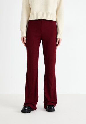 Pantalons évasés côtelés bordeaux en tricot texturé. Associés à un pull crème, avec une silhouette droite et une taille élastique.